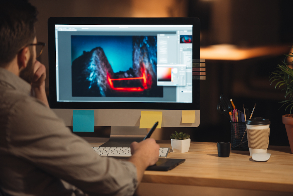 Young concentrated bearded web designer working on computer